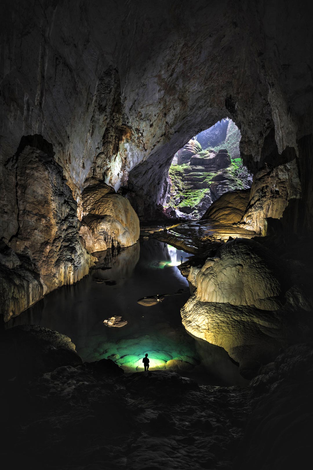 La rivière souterraine de Hang Son Doong éclairée par un puits de lumière et la torche d'un explorateur.